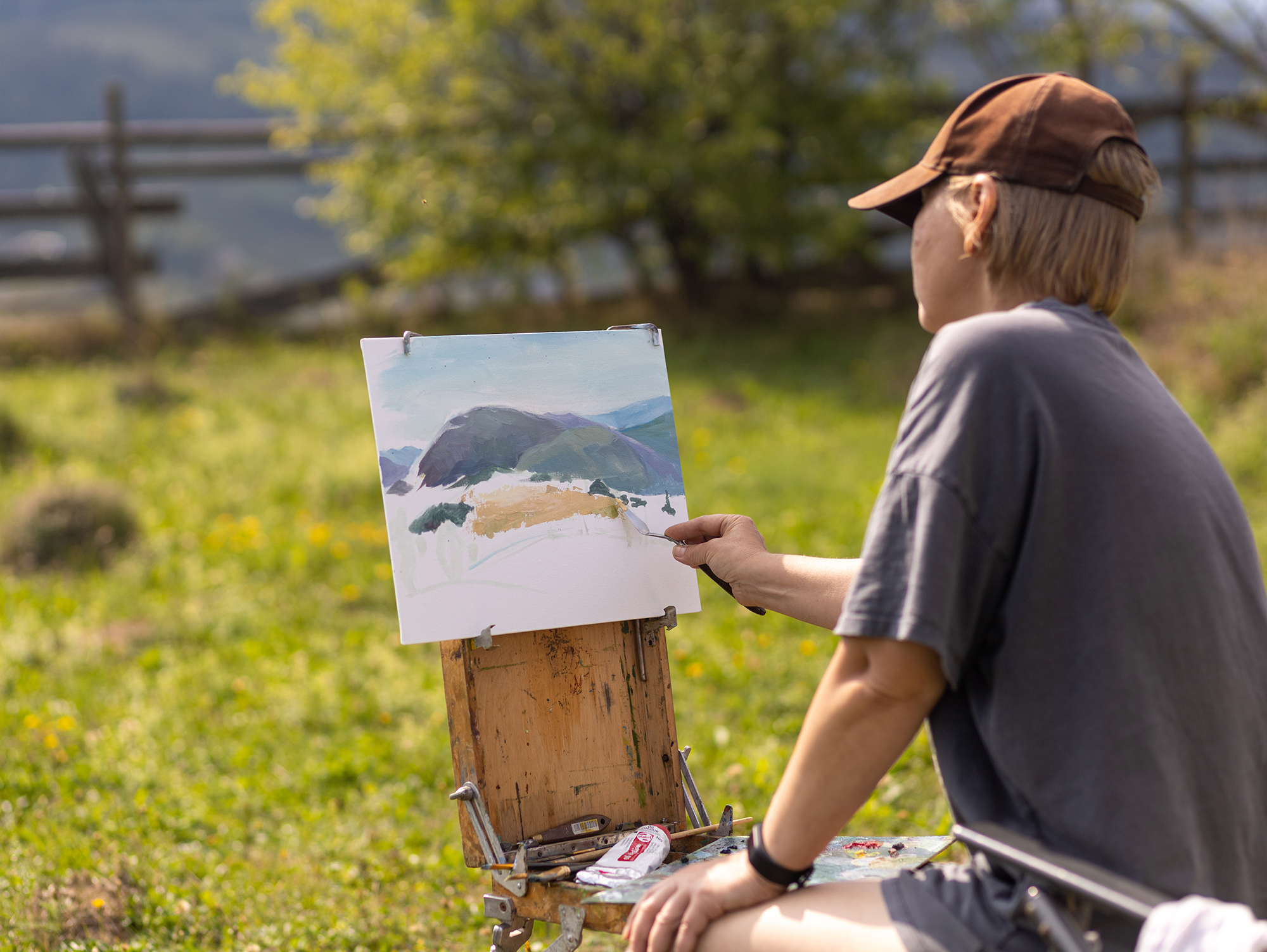 Female artist creates landscape painting in a tranquil meadow surrounded by majestic mountains during a sunny day person painting outdoors in a serene environment